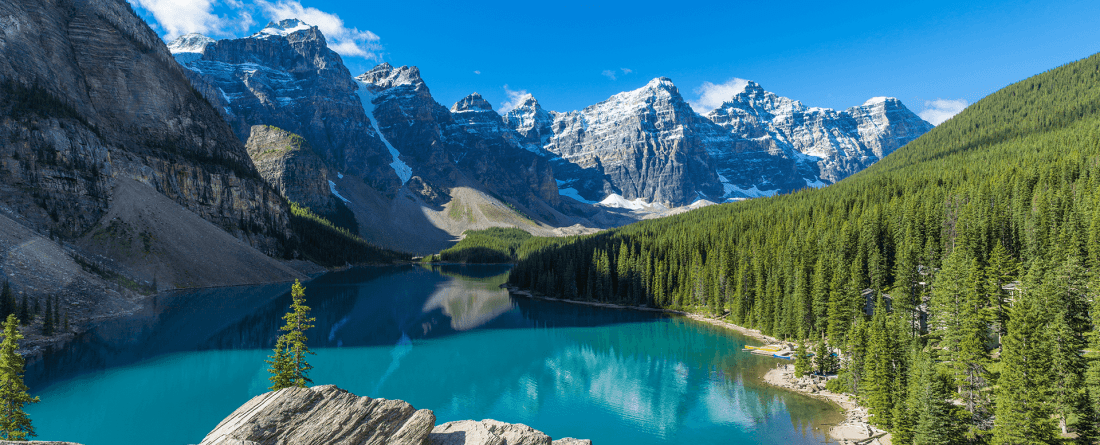 A blue lake with mountains in the background and a forested hillside to the right. 