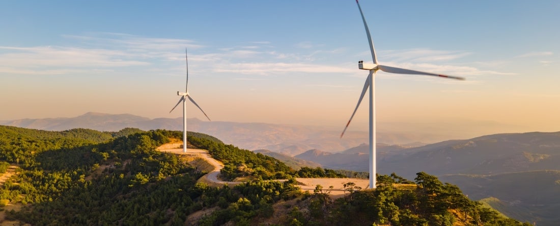 a line of 3 wind turbines on top of a mountain range during the day.
